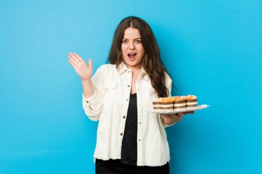 Elinde kek tutan kıvrımlı genç kadın şaşırdı ve şok oldu..