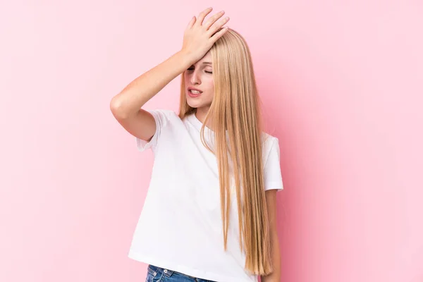 Young blonde woman on pink background forgetting something, slapping forehead with palm and closing eyes.