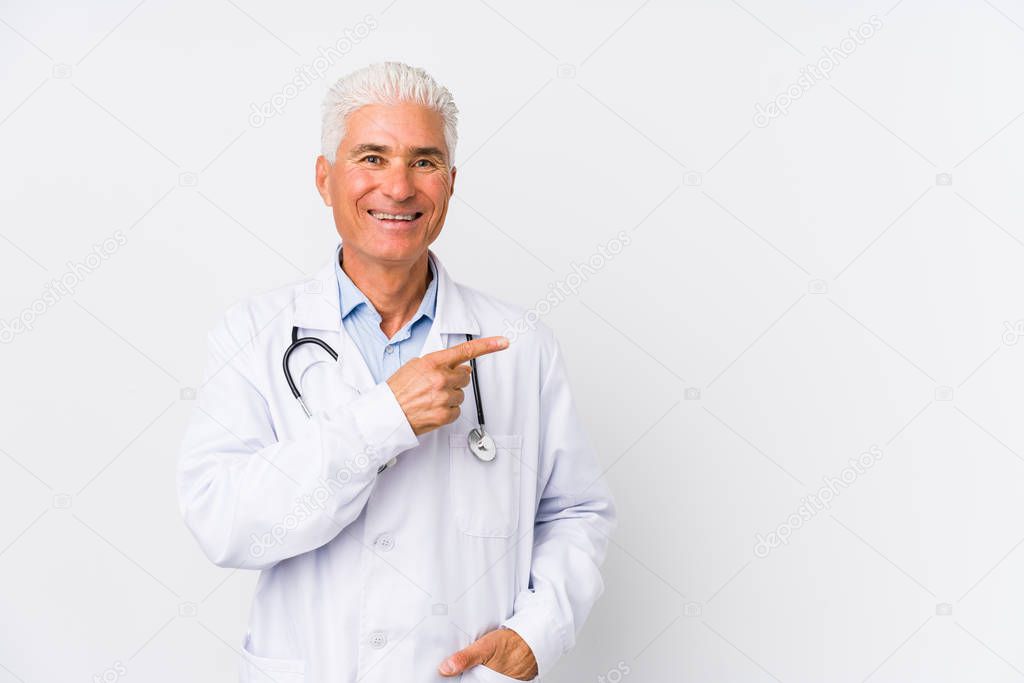 Mature caucasian doctor man smiling and pointing aside, showing something at blank space.