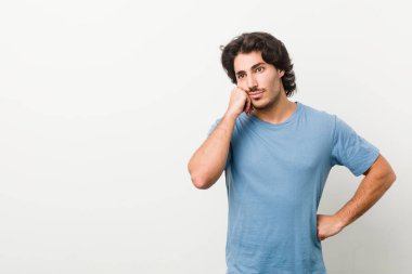 Beyaz bir arkaplan karşısında üzgün ve dalgın hisseden genç ve yakışıklı bir adam, kopyalama alanına bakıyor..