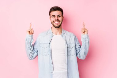 Beyaz arka planda poz veren beyaz tenli genç iş adamı iki ön parmağı da boş bir alan gösteriyor.