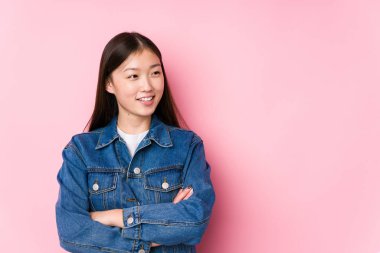 Pembe arka planda poz veren genç Çinli kadın izole edilmiş, kollarını kavuşturup gülümsüyor..