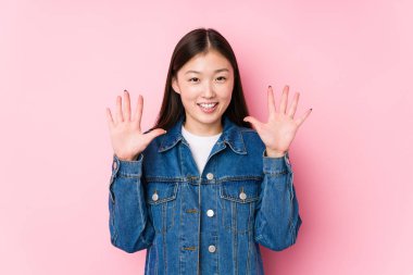 Pembe arka planda poz veren genç Çinli kadın 10 numarayı elleriyle gösteriyor..