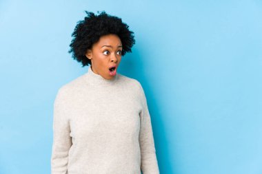 Orta yaşlı Afro-Amerikalı bir kadın mavi arka planda, gördüğü bir şey yüzünden şok olmuş..