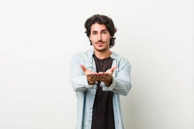 Beyaz arka planda genç yakışıklı bir adam elinde avuç içi bir şeyle kameraya sunuyor..