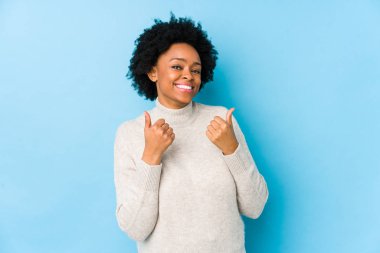 Orta yaşlı Afrikalı Amerikalı bir kadın, mavi bir geçmişe sahip, soyutlanmış, iki parmağını da kaldırmış, gülümseyen ve kendinden emin..