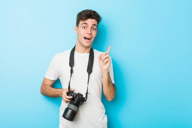Kafkasyalı genç fotoğrafçı elinde kamerayla gülümseyerek işaret parmağıyla işaret ediyor..