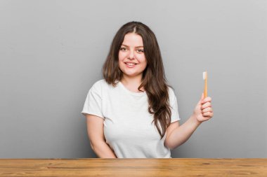 Genç ve kıvrımlı kadın elinde diş fırçası tutarken mutlu, güler yüzlü ve neşeli..