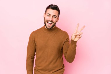 Pembe arka planda yaşayan beyaz bir adam neşeli ve tasasız bir şekilde parmaklarıyla barış sembolü gösteriyor..