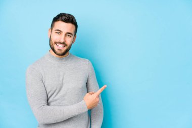Mavi arka planda genç beyaz bir adam izole edilmiş gülümsüyor ve boş alanda bir şeyler gösteriyor..