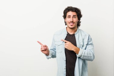 Beyaz arkaplanı olan genç yakışıklı bir adam işaret parmağıyla fotokopi alanını işaret ederek şok oldu..