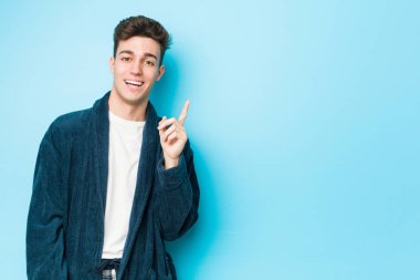 Pijama giyen genç beyaz adam işaret parmağıyla işaret ederek gülümsüyor..