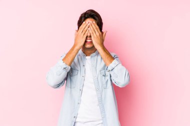 Pembe arka planda poz veren beyaz bir genç yalnız gözlerini elleriyle kapatıyor, gülümseyerek bir sürpriz bekliyor..