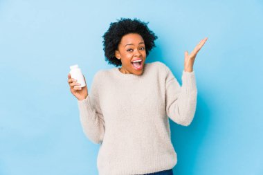 Orta yaşlı Afro-Amerikalı kadın elinde bir vitamin şişesiyle zaferi veya başarıyı kutluyor.