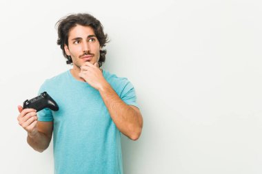 Şüpheli ve şüpheci ifade ile yana bakan bir oyun denetleyicisi tutan genç adam.