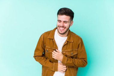 Genç yakışıklı adam mutlu bir şekilde gülüyor ve ellerini karnının üstünde tutarak eğleniyor..