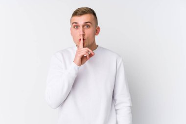 Beyaz arka plandaki genç beyaz adam ya sır saklıyor ya da sessizlik istiyor..