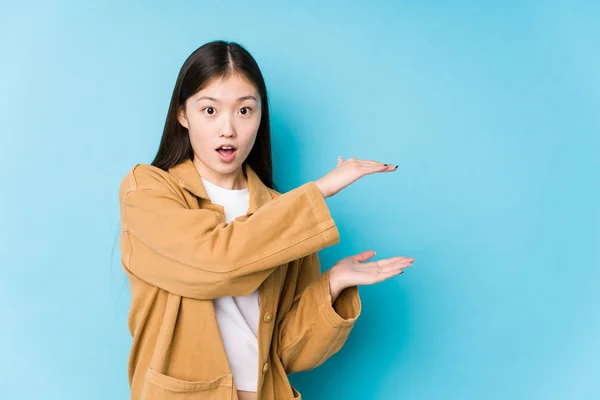 Joven Mujer China Posando Fondo Azul Aislado Sorprendido Sorprendido Sosteniendo —  Fotos de Stock