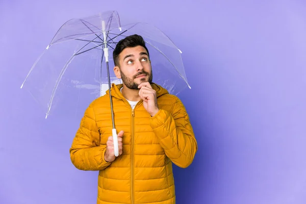 年轻英俊的男子拿着一把雨伞 面带怀疑和怀疑的表情 孤零零地望着一边 — 图库照片