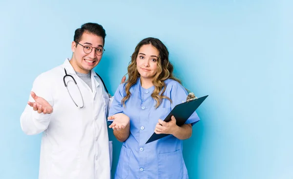 Young Doctor Couple Posing Blue Background Isolated Doubting Shrugging Shoulders — Stock Photo, Image