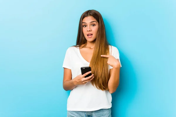 Joven Mujer Caucásica Sosteniendo Teléfono Sorprendido Señalándose Mismo Sonriendo Ampliamente —  Fotos de Stock