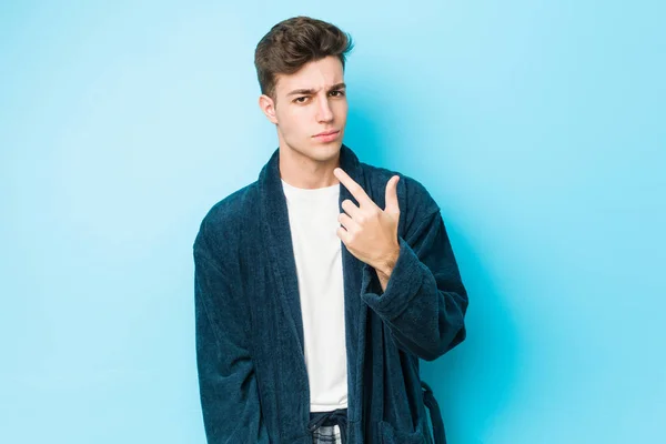 Young caucasian man wearing pajamas pointing with finger at you as if inviting come closer.