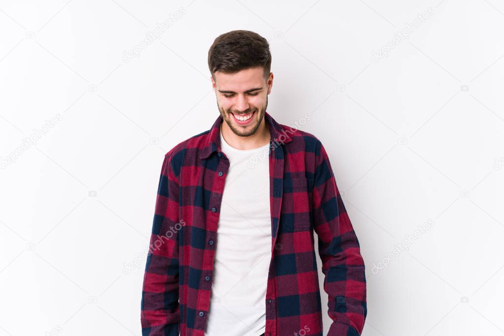 Young caucasian man posing in a white background isolated laughs and closes eyes, feels relaxed and happy.
