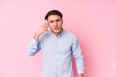 Pembe arka planda poz veren genç beyaz adam işaret parmağıyla hayal kırıklığı gösteriyor..