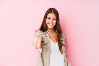 Pembe arka planda poz veren beyaz bir kadın kameraya elini uzatarak selam veriyor..