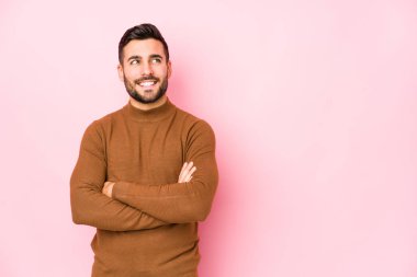 Pembe arka planda genç, beyaz bir adam izole edilmiş, kollarını kavuşturarak gülümsüyor..