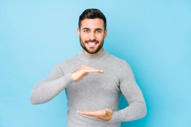 Mavi arka planda genç beyaz adam iki eliyle bir şey tutuyor, ürün sunumu..