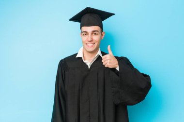 Genç beyaz adam gülümseyerek mezun oldu ve parmağını kaldırdı.