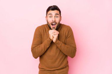 Pembe arka planda genç beyaz bir adam yalnız başına şans diliyor, şaşırıyor ve ağzını açıyor..