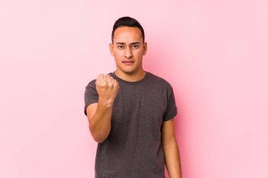 Pembe arka planda poz veren yog latin adam yumruğunu kameraya gösteriyor, agresif yüz ifadesi var..