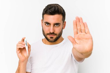Young caucasian man holding a thermometer isolated Young caucasian man holding  a standing with outstretched hand showing stop sign, preventing you.