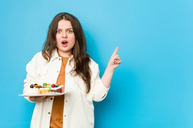 Genç, kıvrımlı bir kadın elinde tatlı bir pasta tutuyor.