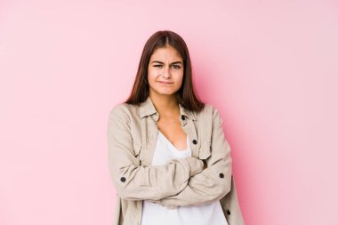 Pembe arka planda poz veren beyaz bir kadın hoşnutsuzca kaşlarını çatıyor, kollarını kavuşturuyor..