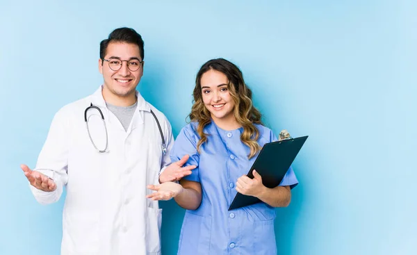 Young Doctor Couple Posing Blue Background Isolated Showing Welcome Expression — 스톡 사진