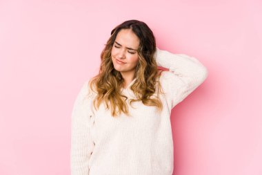 Pembe arka planda poz veren kıvrımlı genç bir kadın sabit yaşam tarzından dolayı boyun ağrısı çekiyor..