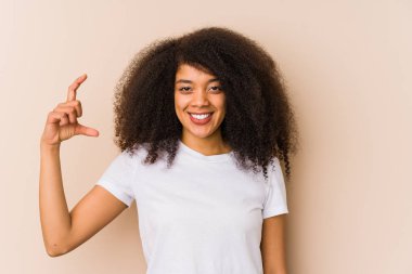 Genç Afrikalı Amerikalı kadın işaret parmaklarıyla küçük bir şey tutuyor, gülümsüyor ve kendinden emin..