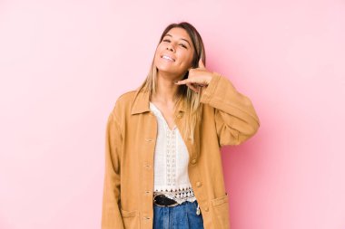 Genç beyaz kadın izole edilmiş poz veriyor. Cep telefonu hareketini parmaklarıyla gösteriyor..