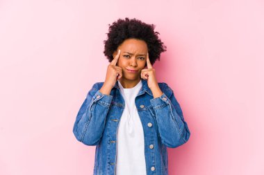 Young african american woman against a pink backgroound isolated focused on a task, keeping forefingers pointing head.