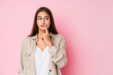 Young caucasian woman posing in a pink background looking sideways with doubtful and skeptical expression.