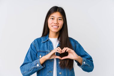 Genç Asyalı kadın gülümsüyor ve elleriyle kalp şeklini gösteriyor..