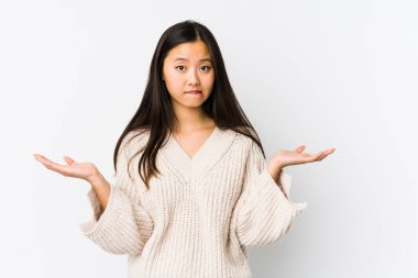 Young chinese woman isolated confused and doubtful shrugging shoulders to hold a copy space.