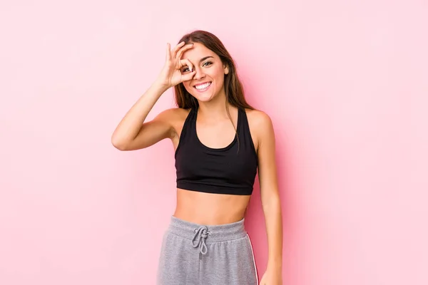年轻的高加索健身女子在粉色背景中摆出一副兴奋的架势 对着眼睛保持着正常的姿势 — 图库照片