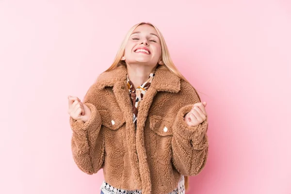 年轻的金发女子 身穿一件外套 背对着粉色背景 举起拳头 感到快乐和成功 胜利的概念 — 图库照片