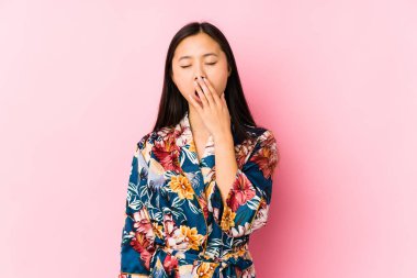 Young chinese woman wearing a kimono pajama isolated yawning showing a tired gesture covering mouth with hand.