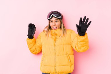 Pembe arka planda kayak kıyafeti giyen beyaz bir kadın, yakın bir tehlike nedeniyle şoka uğruyor.