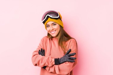 İzole edilmiş kayak kıyafetleri giyen genç beyaz bir kadın. Kendini güvende hissediyor, kararlılıkla kollarını kavuşturuyor..